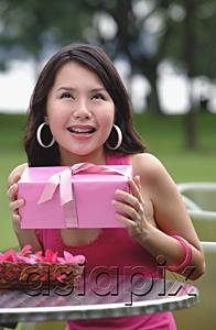 AsiaPix - Woman sitting at outdoor cafe, holding pink gift, looking up
