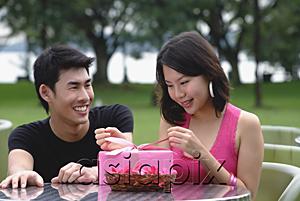 AsiaPix - Woman unwrapping a gift, man crouching next to her, smiling