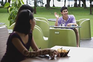AsiaPix - Young man sitting at outdoor cafe, waving at women in the foreground