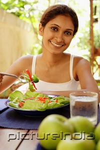 PictureIndia - Woman eating salad, looking at camera