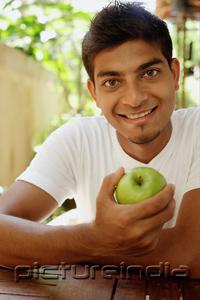PictureIndia - Man holding apple, looking at camera