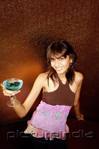 PictureIndia - Young woman holding drink, smiling at camera