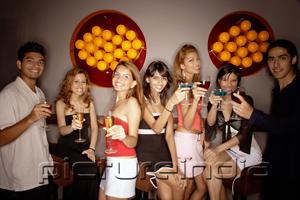 PictureIndia - Young adults in night club, holding drinks out towards camera