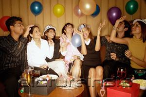PictureIndia - Young adults sitting side by side, celebrating, playing with balloons