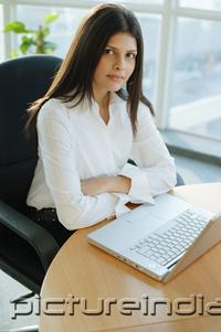 PictureIndia - Female executive sitting, arms crossed, laptop in front of her
