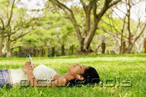 PictureIndia - Young woman lying on grass with headphones