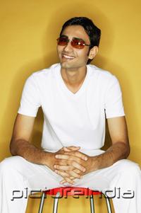 PictureIndia - Young man sitting on stool, wearing sunglasses