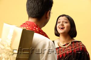 PictureIndia - Indian couple in traditional clothing, standing face to face, man hiding gift behind back