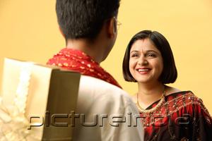 PictureIndia - Indian couple standing face to face, man hiding gift behind back, woman smiling