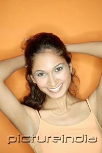 PictureIndia - Young woman in orange tank top, pulling hair back