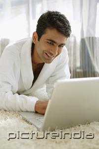 PictureIndia - Man in bathrobe, using laptop, smiling