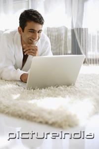 PictureIndia - Man in bathrobe, using laptop, hand on chin, smiling