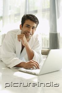 PictureIndia - Man in bathrobe, using laptop, hand on chin, smiling at camera