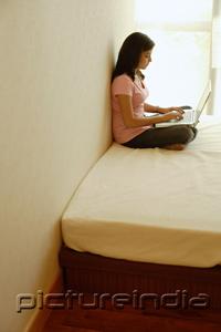 PictureIndia - Woman at home, sitting on bed, using laptop