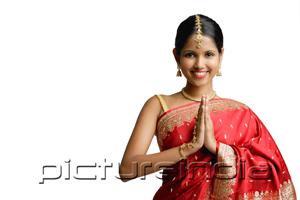 PictureIndia - Woman in red sari, standing with hands together, smiling at camera