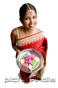 PictureIndia - Woman in sari, holding plate of Indian cakes, smiling at camera