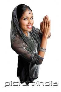 PictureIndia - Woman in gray sari standing against white background, hands together